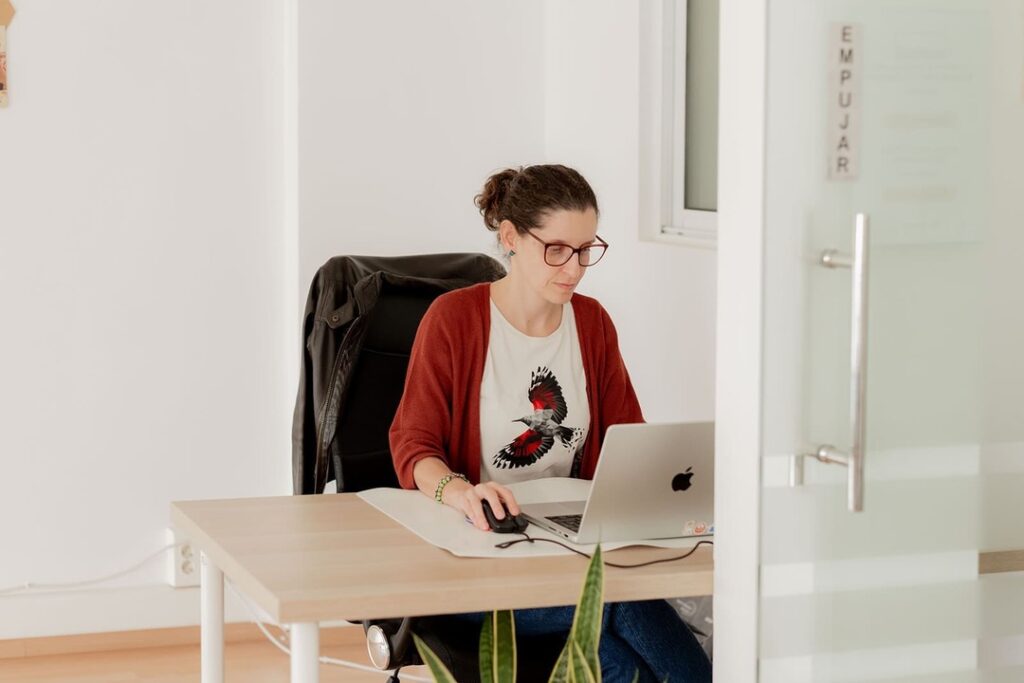Mujer trabajando con su portátil en un puesto flexible dentro de un coworking, en un espacio luminoso y tranquilo.